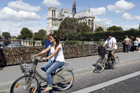 A couple ride on Velib self-service public bicycles on the Pont de l'Archeveche bridge, which is covered with thousands of padlocks, or love locks, near the Notre Dame Cathedral in Paris, August 22, 2014. France kept its title as the world's top tourist d
