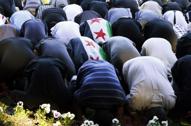 Two Muslims covered with the Syrian opposition flag pray