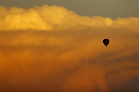 A hot air balloon floats past a distant thunderstorm