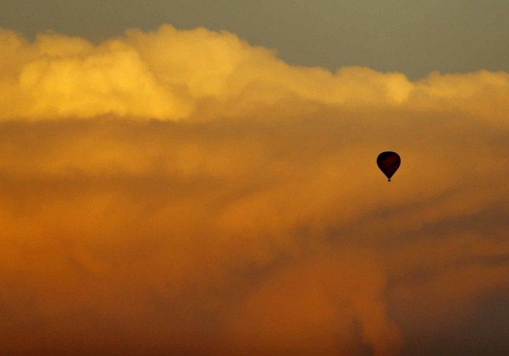 A hot air balloon floats past a distant thunderstorm