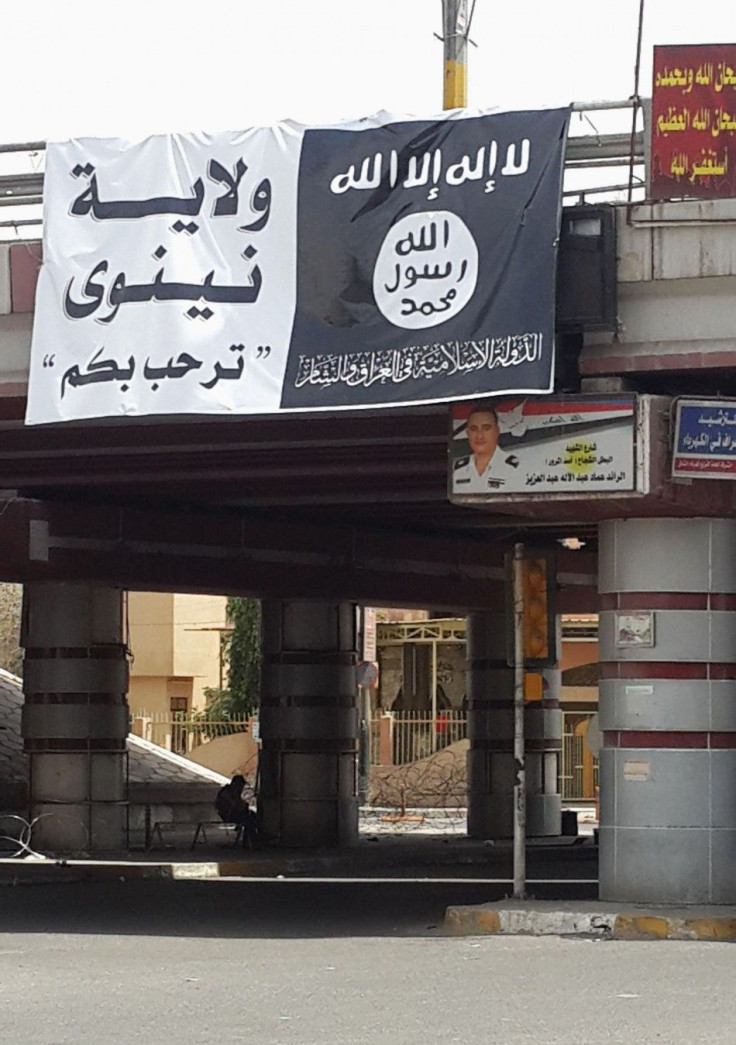 A man sits under a sign with flag belonging to the Islamic State in Iraq and the Levant (ISIL) along a street in the city of Mosul June 12, 2014. 