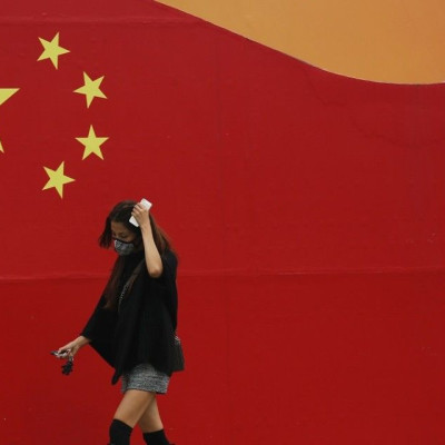 A woman wearing a mask walks past a wall painted with China's national flag in central Beijing, October 9, 2014. Beijing issued a yellow alert for air pollution on Wednesday with smog forecast to continue for the next three days until Saturday, said the B