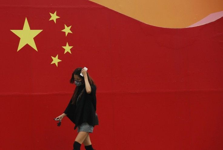 A woman wearing a mask walks past a wall painted with China's national flag in central Beijing, October 9, 2014. Beijing issued a yellow alert for air pollution on Wednesday with smog forecast to continue for the next three days until Saturday, said the B