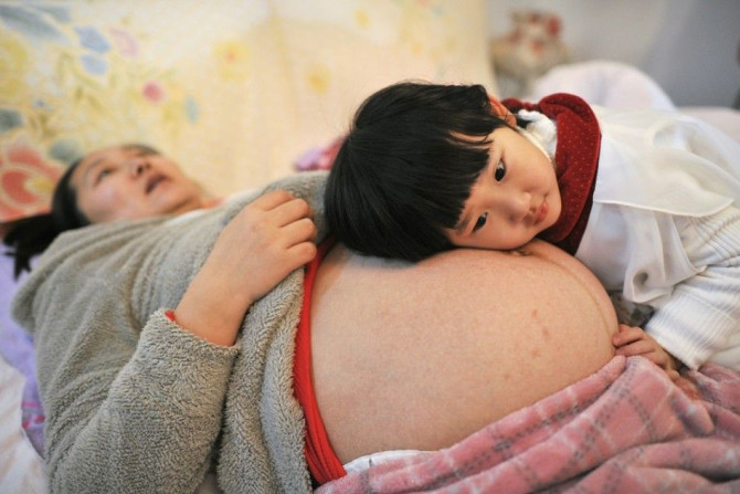 Li Yan (L), pregnant with her second child, lies on a bed as her daughter places her head on her mother's stomach in Hefei, Anhui province February 20, 2014. Li gave birth to a baby boy on February 23, 2014 after Li's family became the first to receive a 
