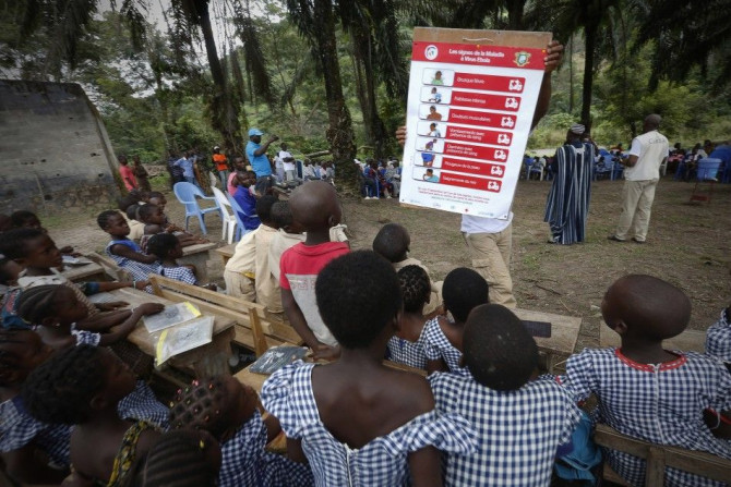 A man shows students a poster on the symptoms of Ebola during a United Nations Children's Fund (UNICEF) Ebola awareness drive in Gueupleu, Man, western Ivory Coast November 3, 2014.