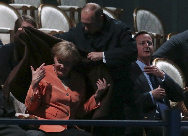 Russia&#039;s President Vladimir Putin (C) places a shawl around German Chancellor Angela Merkel
