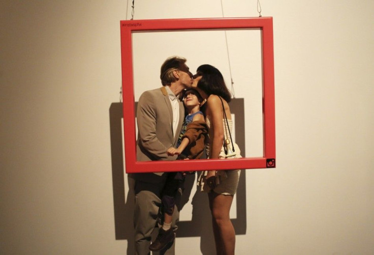 A couple kisses while holding their son as they pose for a portrait during Sao Paulo Fashion Week November 3, 2014.REUTERS/Nacho Doce