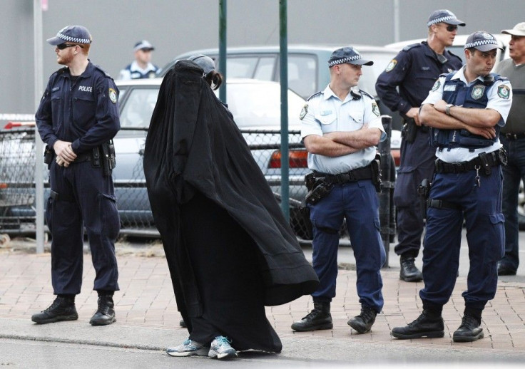 Police officers stand on guard next to a woman wearing a burqa