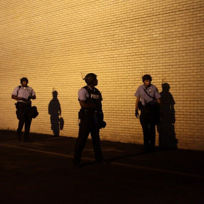 Police officers in riot gear watch demonstrators protesting against the shooting of Michael Brown from the side of a building in Ferguson, Missouri August 19, 2014.