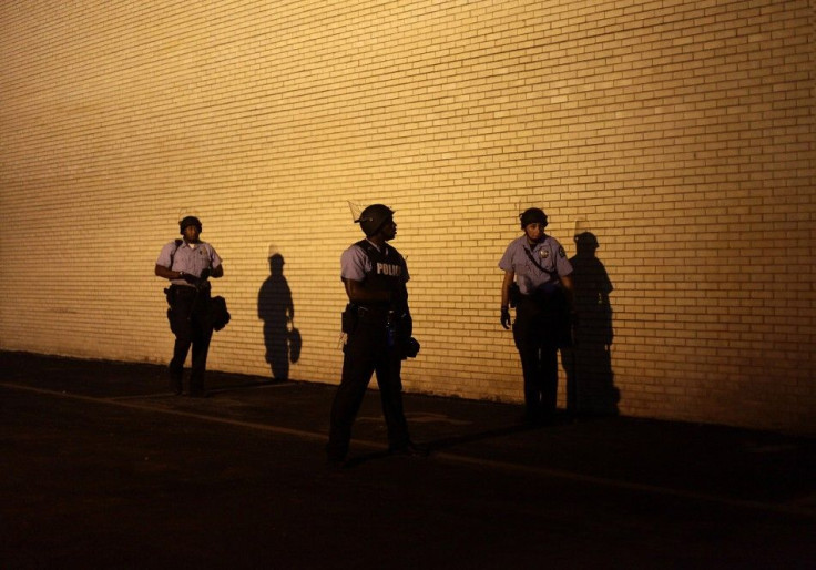 Police officers in riot gear watch demonstrators protesting against the shooting of Michael Brown from the side of a building in Ferguson, Missouri August 19, 2014.