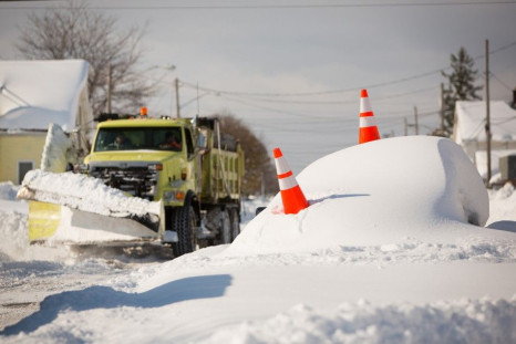 An abandoned car marked by orange cones is buried under snow as a snowplow passes by in Buffalo, New York, November 19, 2014.