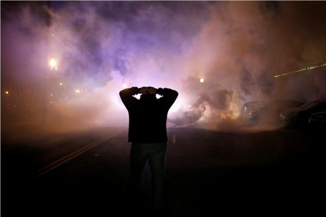 A protester stands with his hands on his head as a cloud of tear gas approaches