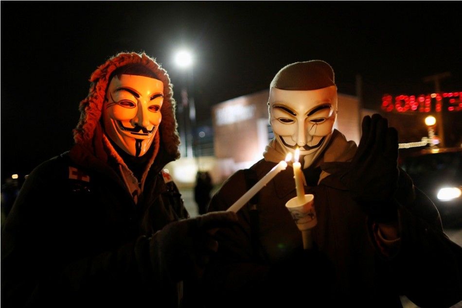 Protesters wearing Guy Fawkes masks take part in a candlelight vigil outside the Ferguson Police Department in Ferguson