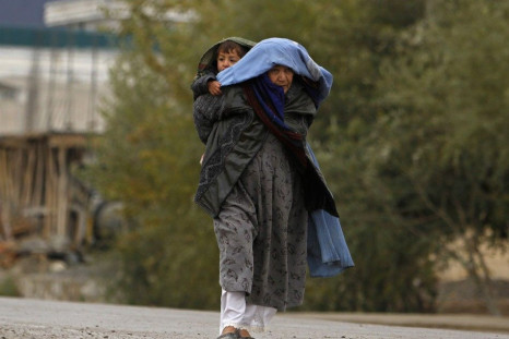 An Afghan woman carries her child on her back as she walks on a road during a rainy day in Kabul November 6, 2013.