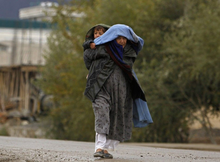 An Afghan woman carries her child on her back as she walks on a road during a rainy day in Kabul November 6, 2013.