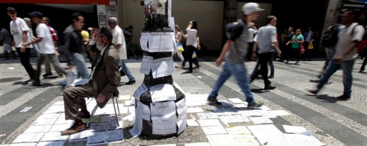 A job promoter sits close to list of job offers posted along a main street in downtown Sao Paulo November 19, 2014. Brazil's unemployment rate fell unexpectedly in October despite widening layoffs in manufacturing and construction, in welcome news for Pre