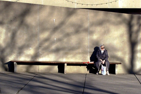 An elderly women sits in the warm sun surrounded by the shadows of winter outside Toronto City Hall