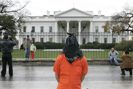 A tourists take souvenir snaps nearby as a hooded protester dressed to represent a detainee of the U.S. government demonstrates against torture outside the White House in Washington