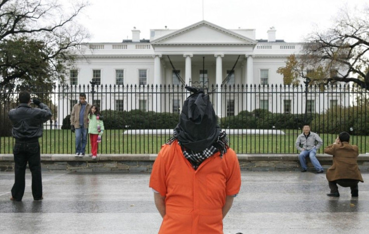 A tourists take souvenir snaps nearby as a hooded protester dressed to represent a detainee of the U.S. government demonstrates against torture outside the White House in Washington