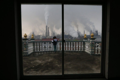 A girl reads a book on her balcony as smoke rises from chimneys of a steel plant, on a hazy day in Quzhou, Zhejiang province April 3, 2014. China's plan for a market in air pollution permits promises to help clean up its air cheaply, but the move cou