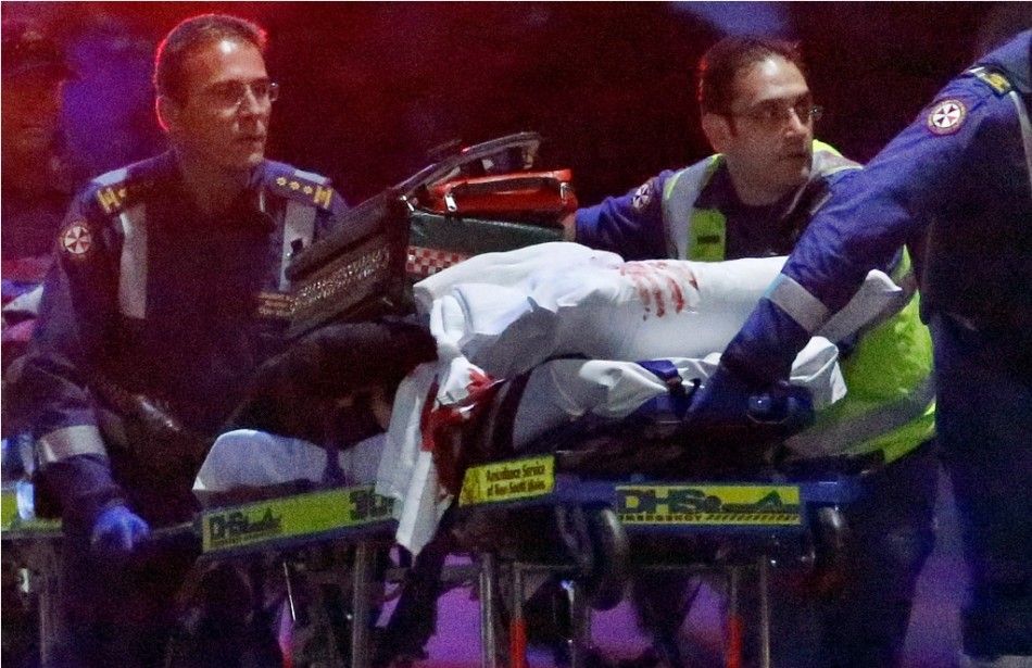 Paramedics remove a person, with bloodstains on the blankets covering the person, on a stretcher from the Lindt cafe