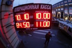 A man stands next to a building under a board showing currency exchange rates in Moscow