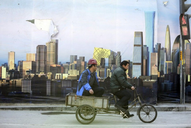 A worker rides past a poster showing Beijing&#039;s central business district outside a construction site in Beijing