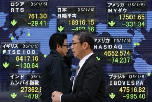 Passersby walk past in front of an electronic board displaying Japan's Nikkei average (top C) and various countries' stock price index outside a brokerage in Tokyo January 6, 2015. Asian shares tumbled on Tuesday as sliding oil prices and political uncert