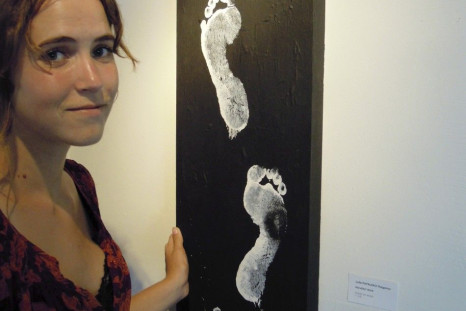 Morgan Wienberg, 22, poses beside a painting of footprints at the Jacmel Gallery in Miami