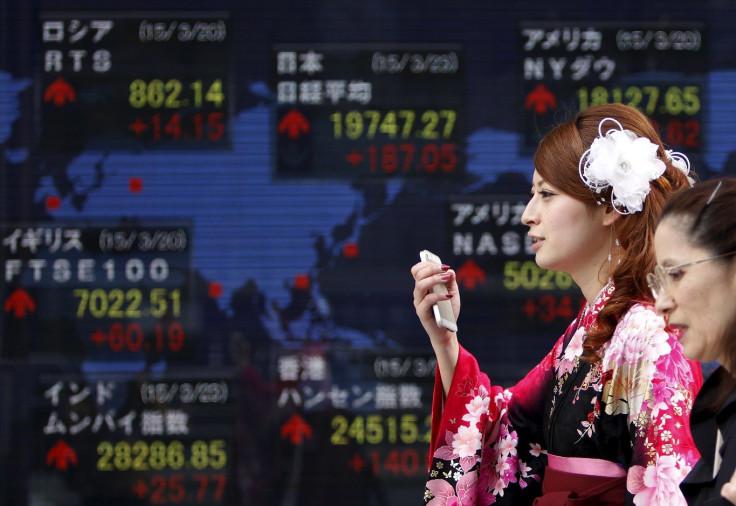 A woman wearing a Hakama, or Japanese traditional Kimono, holds her mobile phone as she walks past an electronic board, showing the stock market indices of various countries, outside a brokerage in Tokyo, March 23, 2015.