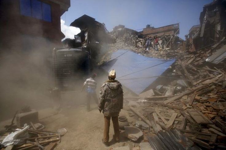 A man looks on amidst rising dust as a damaged house is brought down