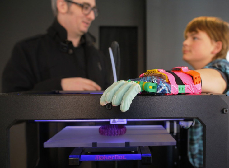 RTX15NH1Twelve-year-old Leon McCarthy (R) rests his prosthetic hand on a MarkerBot Replicator 2 Desktop 3D Printer