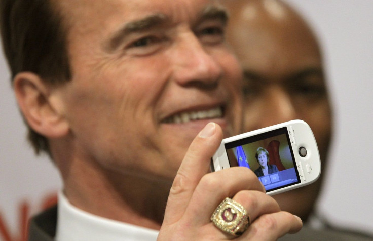 California Governor Arnold Schwarzenegger holds a Google phone displaying a podcast of German Chancellor Angela Merkel