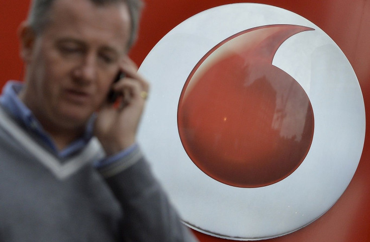 A man speaks on a mobile phone as he walks past Vodafone branding outside a retail store in London November 12, 2013.
