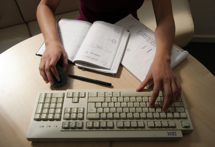 A generic picture of a woman working in an office sitting at her desk typing on a computer.