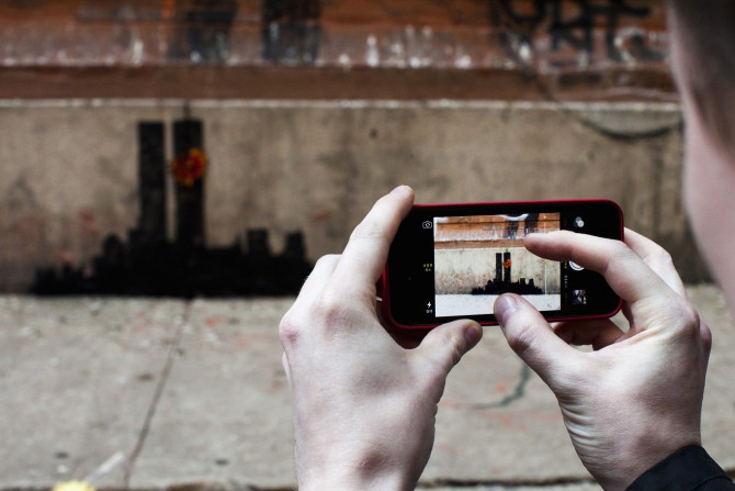 A man takes a picture of an artwork by British graffiti artist Banksy at Lower Manhattan in New York, October 15, 2013.