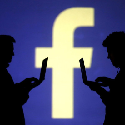 FILE PHOTO: Silhouettes of laptop users are seen next to a screen projection of Facebook logo in this picture illustration taken March 28, 2018.