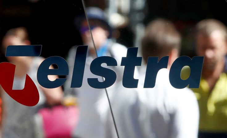 Pedestrians walk behind a Telstra logo in Sydney, Australia, February 8, 2018.