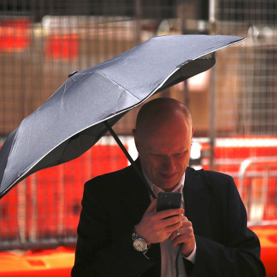 A man uses his phone as he holds an umbrella crossing a street in the central business district (CBD) of Sydney in Australia, February 13, 2018.