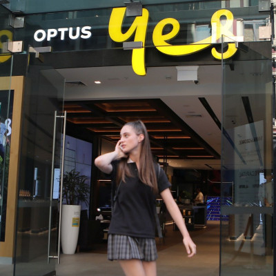 A woman uses her mobile phone as she walks past in front of an Optus shop in Sydney, Australia, February 8, 2018.