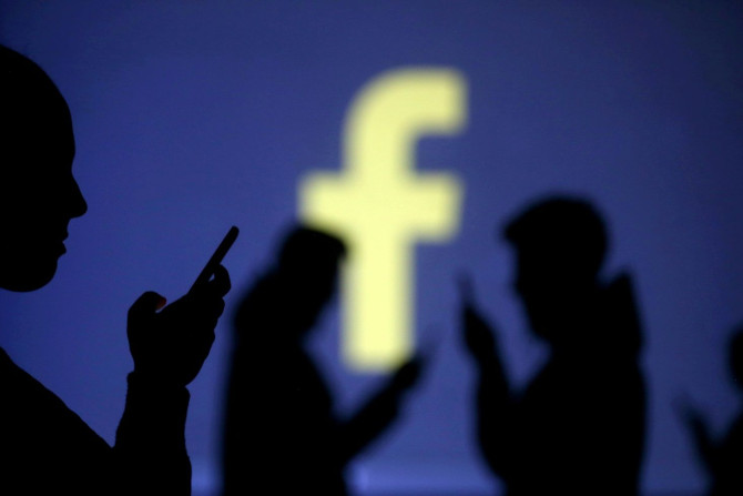 FILE PHOTO: Silhouettes of mobile users are seen next to a screen projection of Facebook logo in this picture illustration taken March 28, 2018.