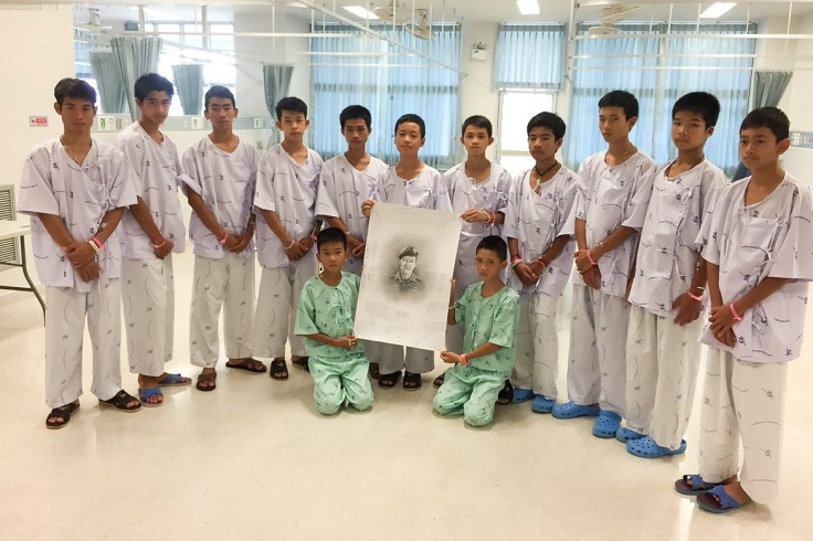The 12-member "Wild Boars" soccer team and their coach rescued from a flooded cave pose with a drawing picture of Samarn Kuna