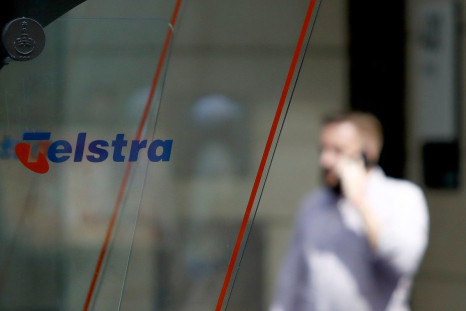 A man uses his mobile phone behind a Telstra logo in central Sydney, Australia, February 8, 2018.