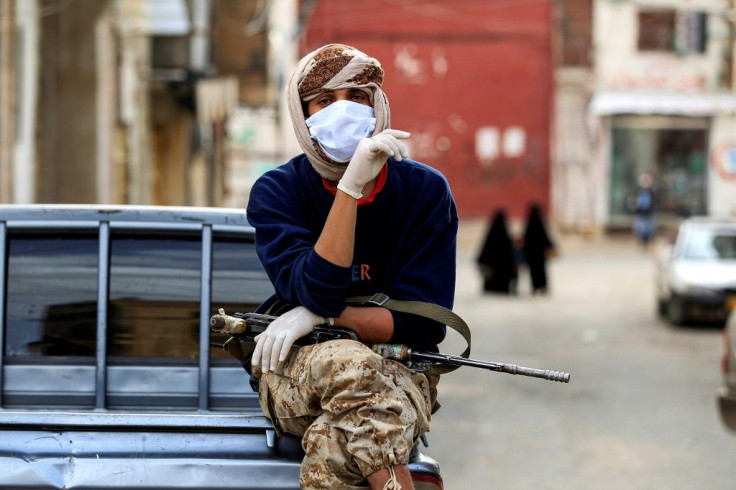 A fighter loyal to the Huthi rebels keeps guard as volunteers take measures to prevent the spread of COVID-19 in Yemen's capital Sanaa