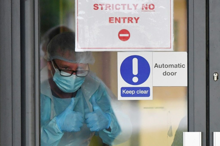 Medical staff signal from behind a door as they participate in a national "clap for carers" to show thanks for the work of Britain's NHS at Aintree University Hospital in Liverpool, northwest England