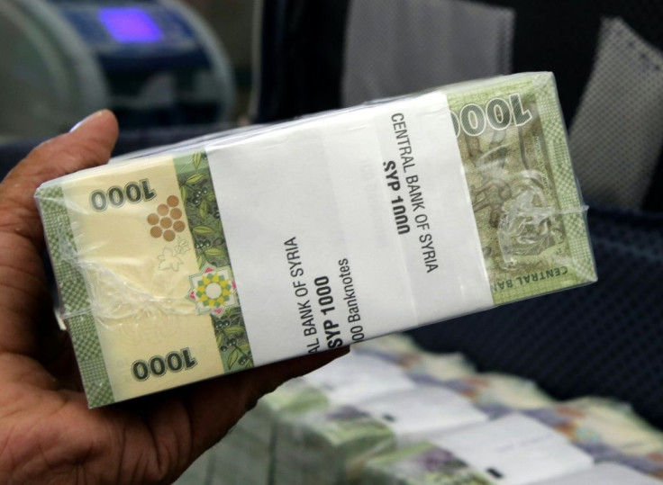 A bank worker in Damascus holds up a bundle of Syrian 1,000-pound bank notes