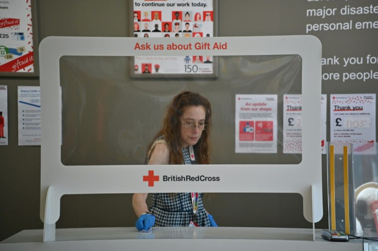 An employee cleans around the till protected by a 'sneeze screen' as a measure against the spread of COVID-19 at a British Red Cross charity shop in London