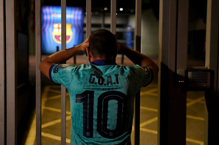 A Barcelona fan in a Lionel Messi jersey peeks through the gate at the club's headquarters