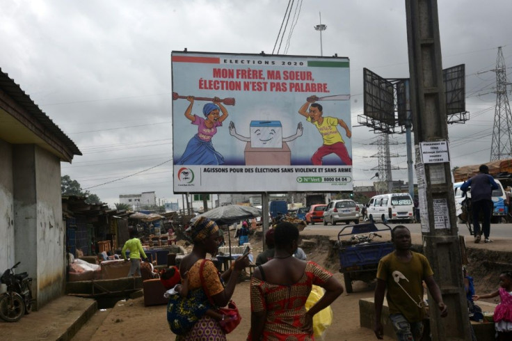 People walk past a billboard in Abidjan urging peaceful elections next month