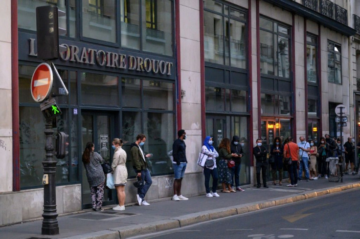 People wearing face masks wait in line in front of a medical laboratory in Paris to get tested for coronavirus